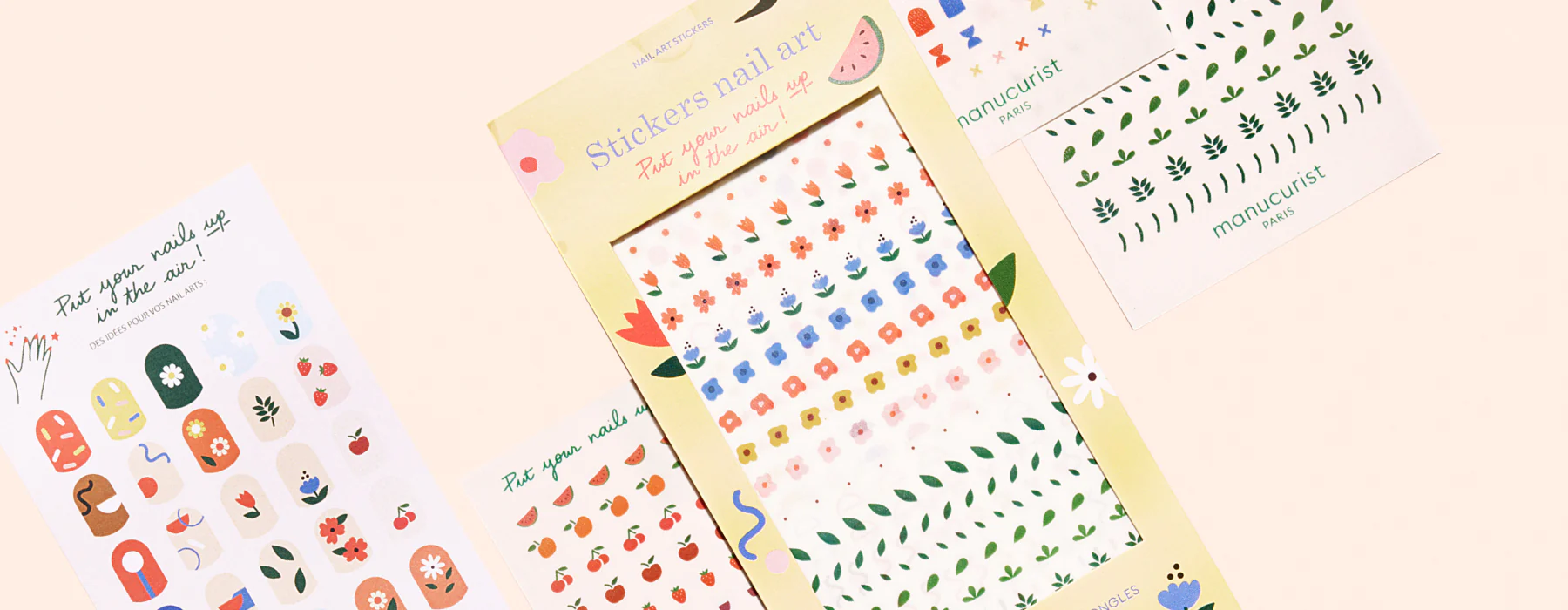 Assorted sheets of colorful nail art stickers featuring flowers, leaves, fruit, and matryoshka doll designs, arranged on a light pink background.
