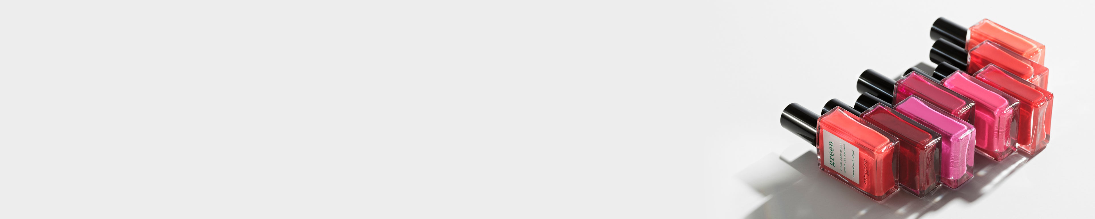 Five bottles of nail polish in various shades of red, pink, and orange are arranged in a diagonal line on a white background, with plenty of empty space on the left.