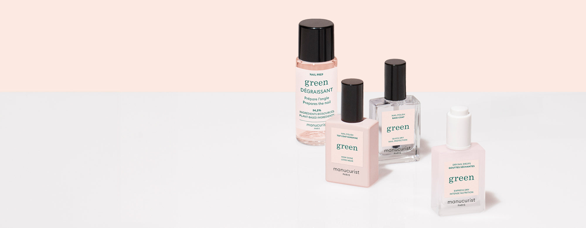 Four manicure products in clear and frosted bottles labeled green by Manucurist are arranged on a white and pale pink background. Products include base, top coat, remover, and nail polish.