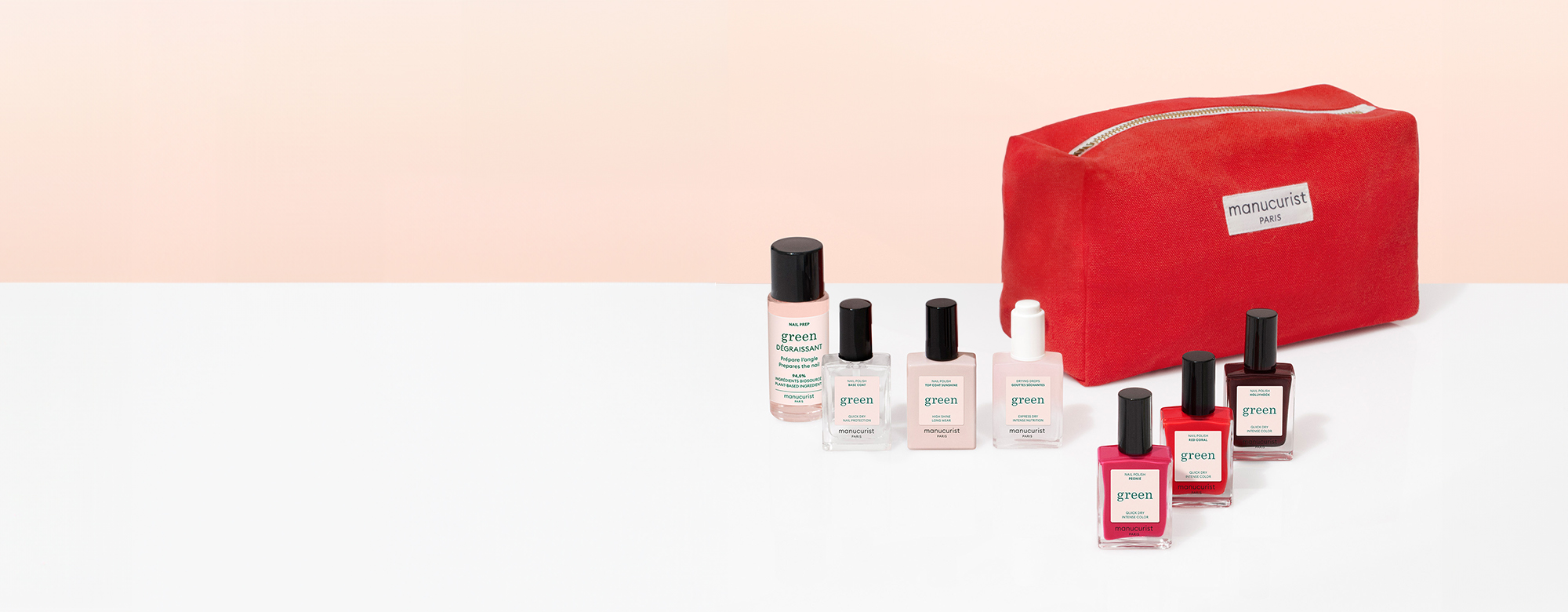 A row of nail polish bottles in various colors is displayed next to a bright red cosmetic bag on a white surface with a pale peach background.