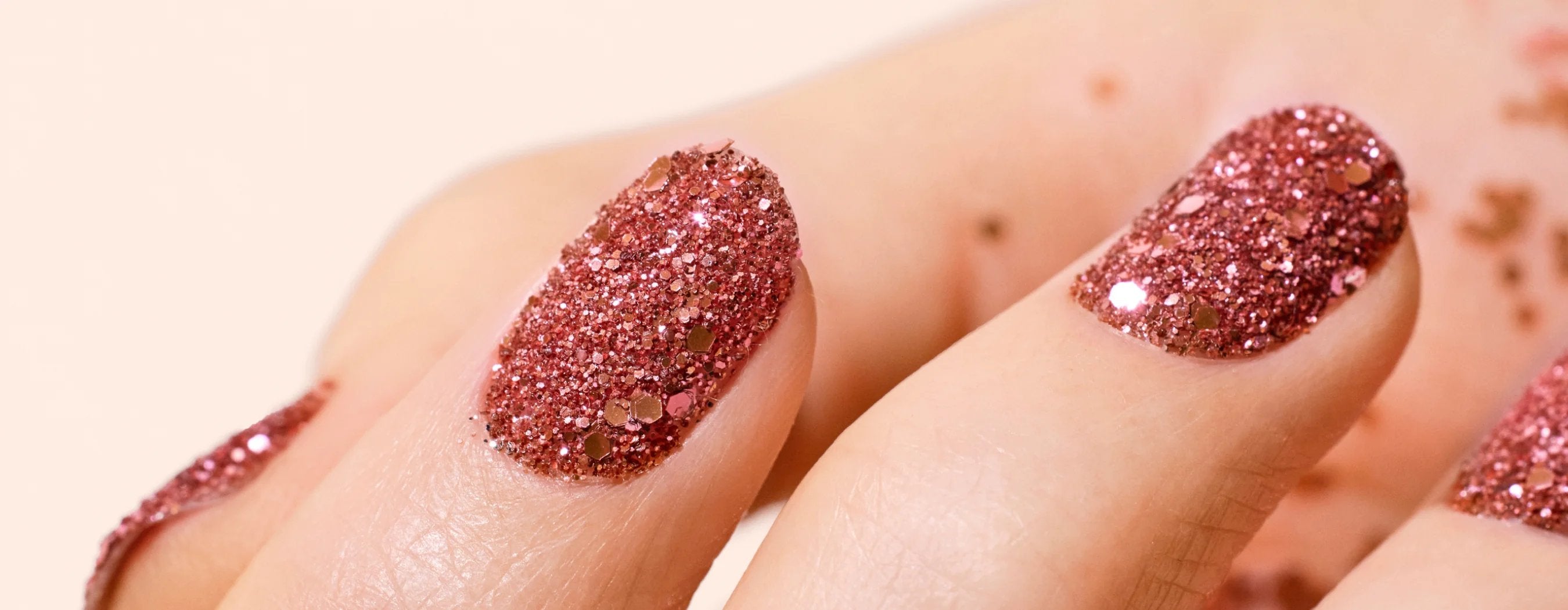 Close-up of fingers with pink glitter nail polish, showing a sparkling, textured finish on neatly manicured nails.