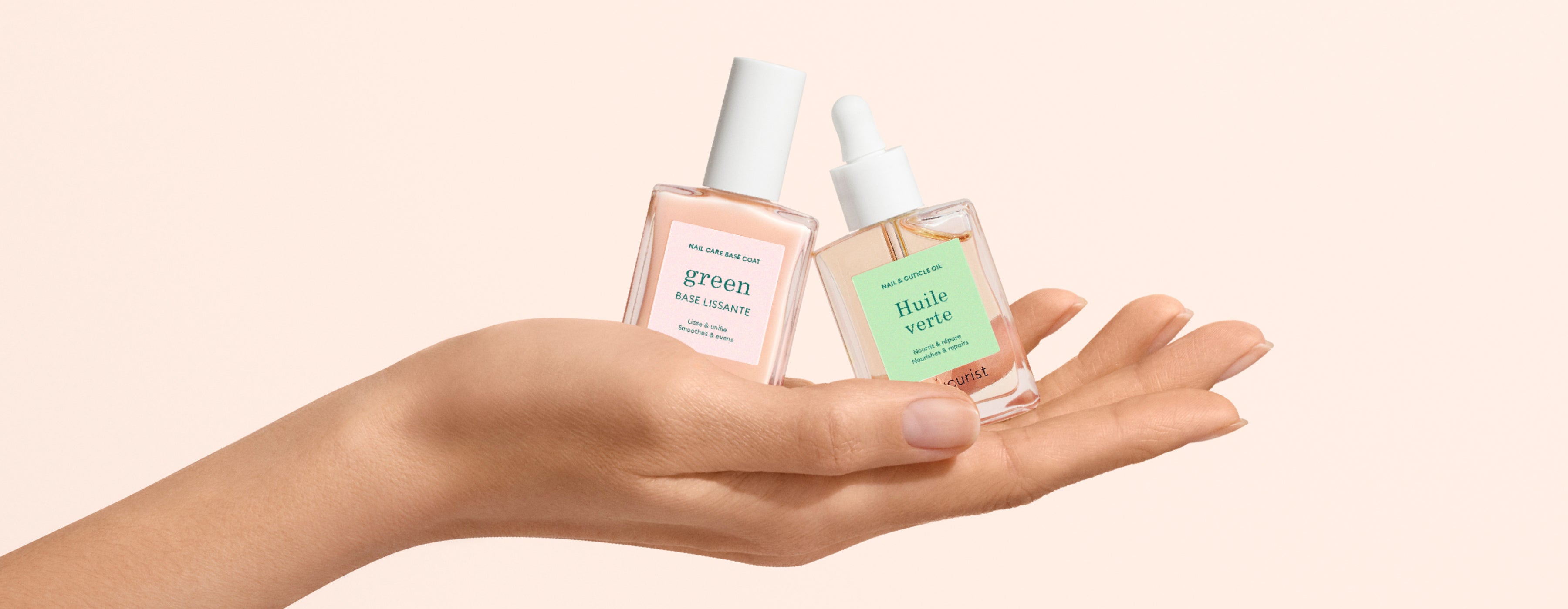 A hand holds two glass skincare bottles with droppers, labeled “green” and “huile verte,” against a light beige background.