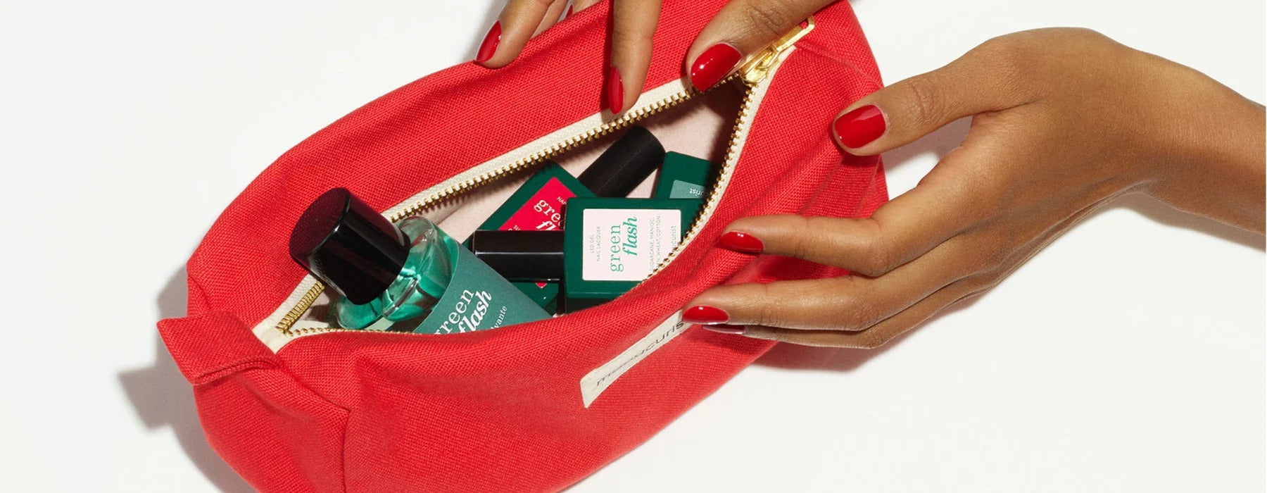 A dark green rectangular pouch with a zipper and a small white-green logo sits on a light pink surface, with a plain light pink background.