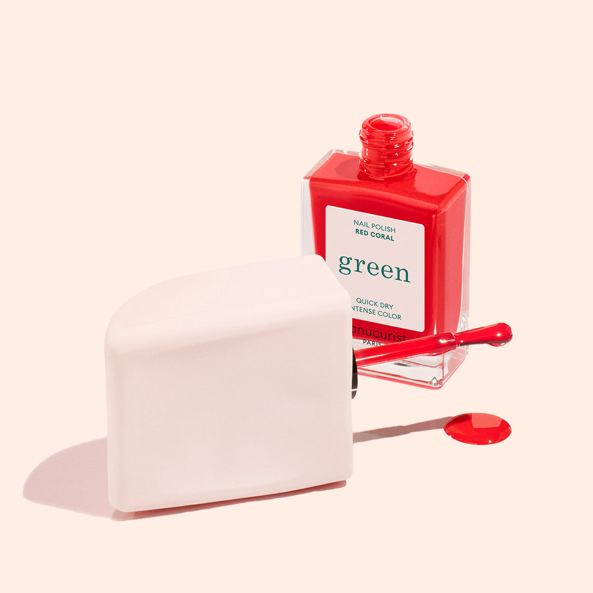 A red Manucurist Mani Helper nail polish bottle stands open, brush resting on a cream object, with a drop of polish suggesting perfect manicure—set against a light beige background.