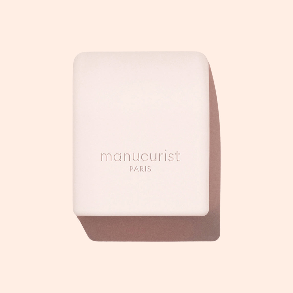 The Manucurist Mani Helper is a pale pink rectangular soap bar with centered embossed text, displayed on a light beige background—it’s ideal for prepping hands before polish or creating the perfect manicure.