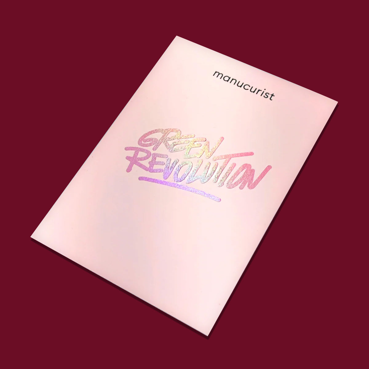 A pale pink Manucurist folder on a burgundy background displays "manucurist" at the top and "GREEN REVOLUTION" in iridescent letters—perfect for gifting with a Manucurist Gift Card.