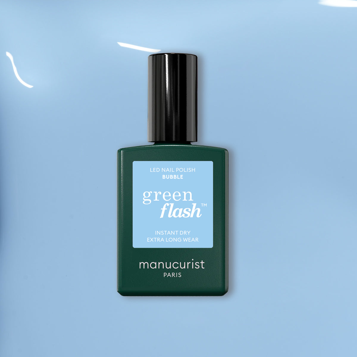 A bottle of Manucurist Bubble Green Flash blue LED gel polish, featuring a dark green base, black cap, and blue label, sits on a shiny light blue surface.