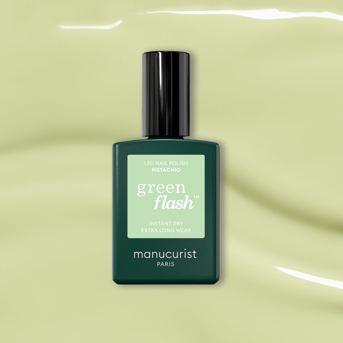 A dark green Manucurist Pistachio Green Flash gel nail polish bottle sits on a glossy light green surface with soft reflections.