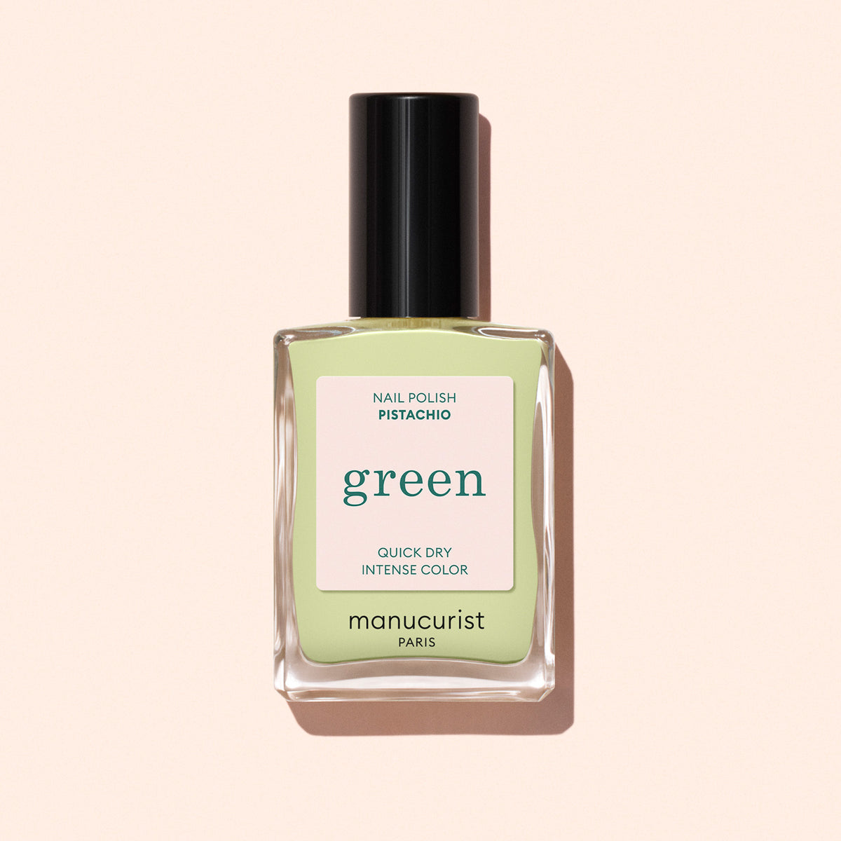 A clear glass bottle of Manucurist nail polish in the Pistachio shade, with a pale green label, black cap, and Quick Dry Intense Color text on a light beige background. Ideal for lovers of pale green nails.