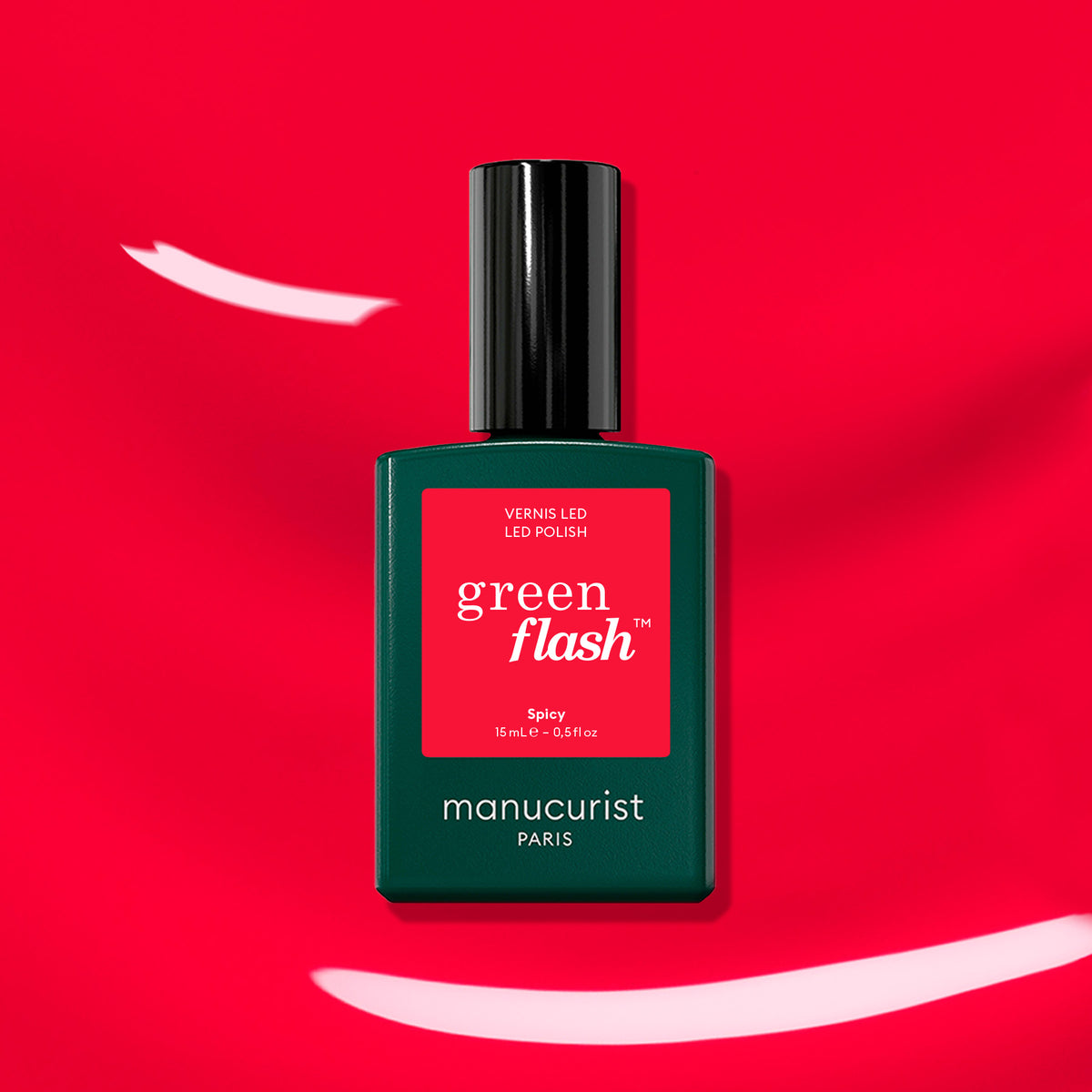 A bottle of Manucurist Spicy nail polish stands out on a bold red background with white brushstrokes, its rectangular shape, black cap, and vivid red label evoking classic eighties style.