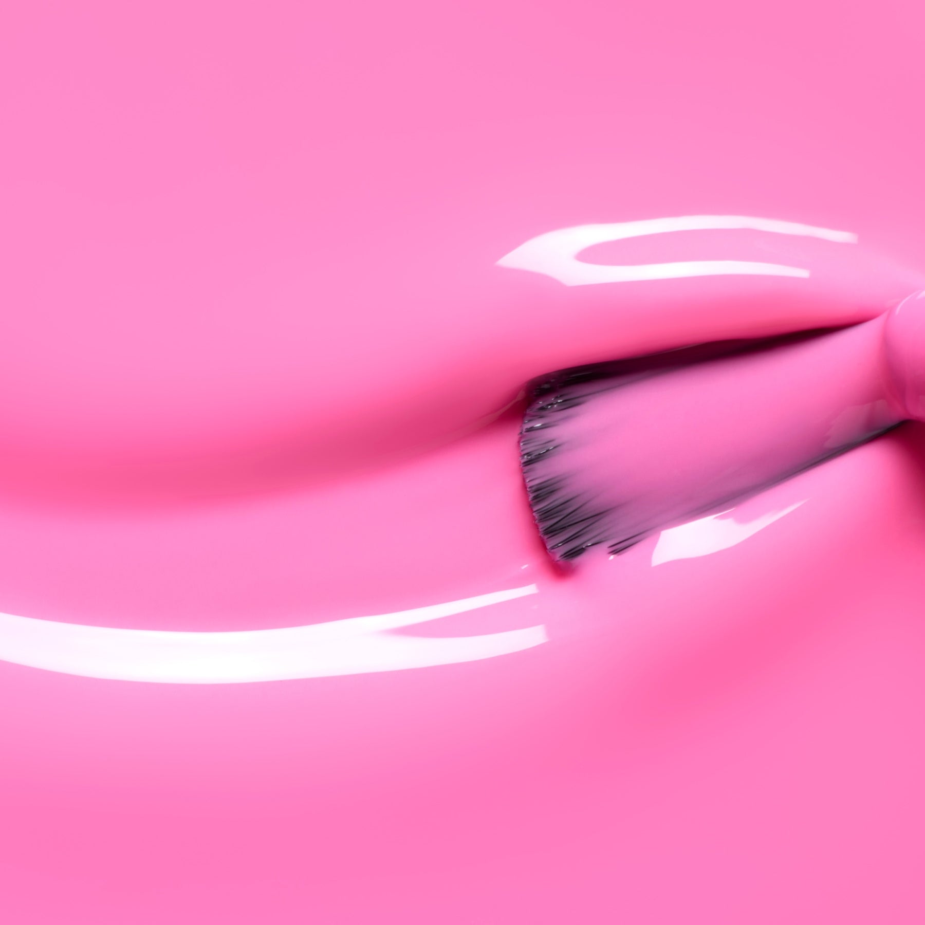 A close-up of a brush applying Bloom by Manucurist—a glossy neon pink polish with subtle blue undertones—creating smooth, shiny streaks on a matching surface from the Green™ range.