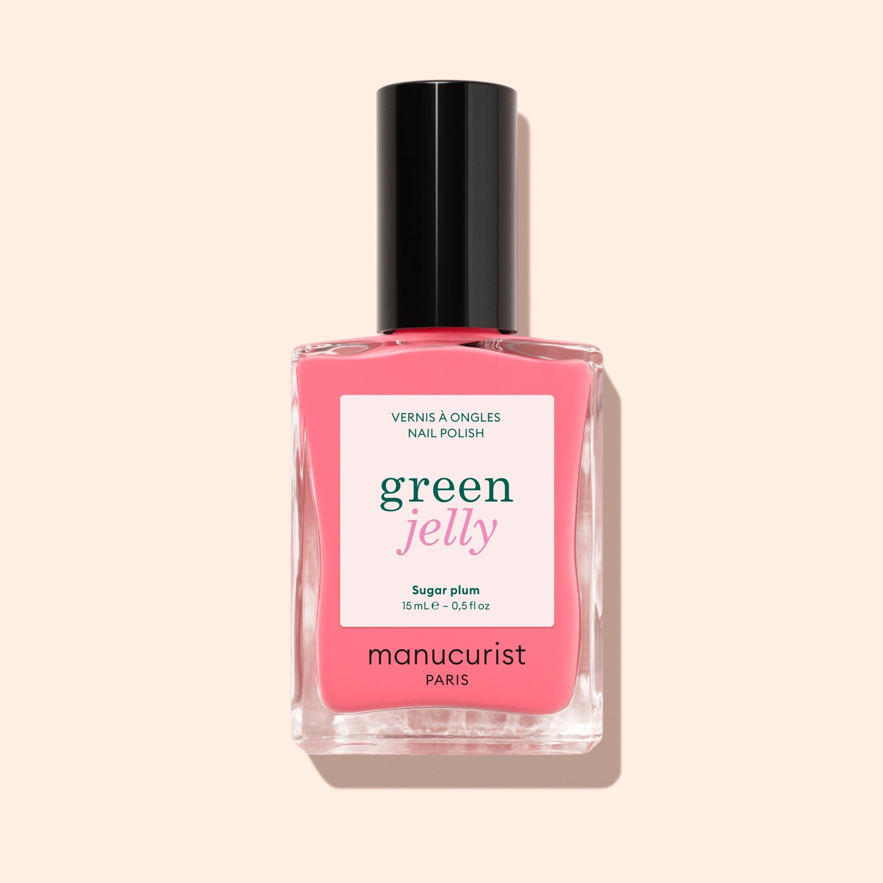 A bottle of Manucurist Sugar Plum nail polish, featuring a translucent pop pink shade with an ultra-glossy finish and a black cap, is shown against a pale pink background.