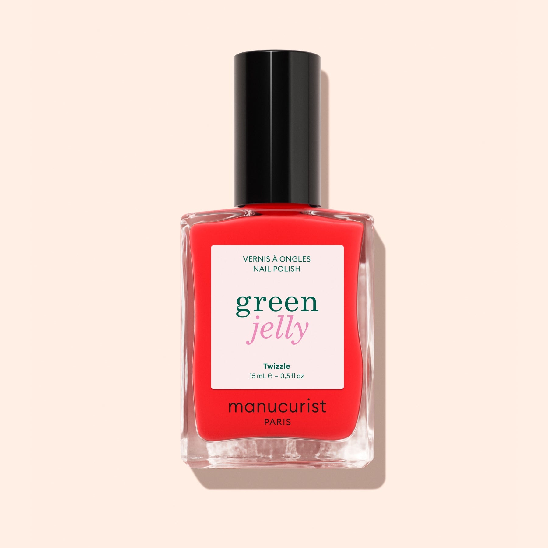 A bottle of ultra-glossy, bright red nail polish labeled Twizzle by Manucurist, with a black cap and white label, set against a pale peach background.