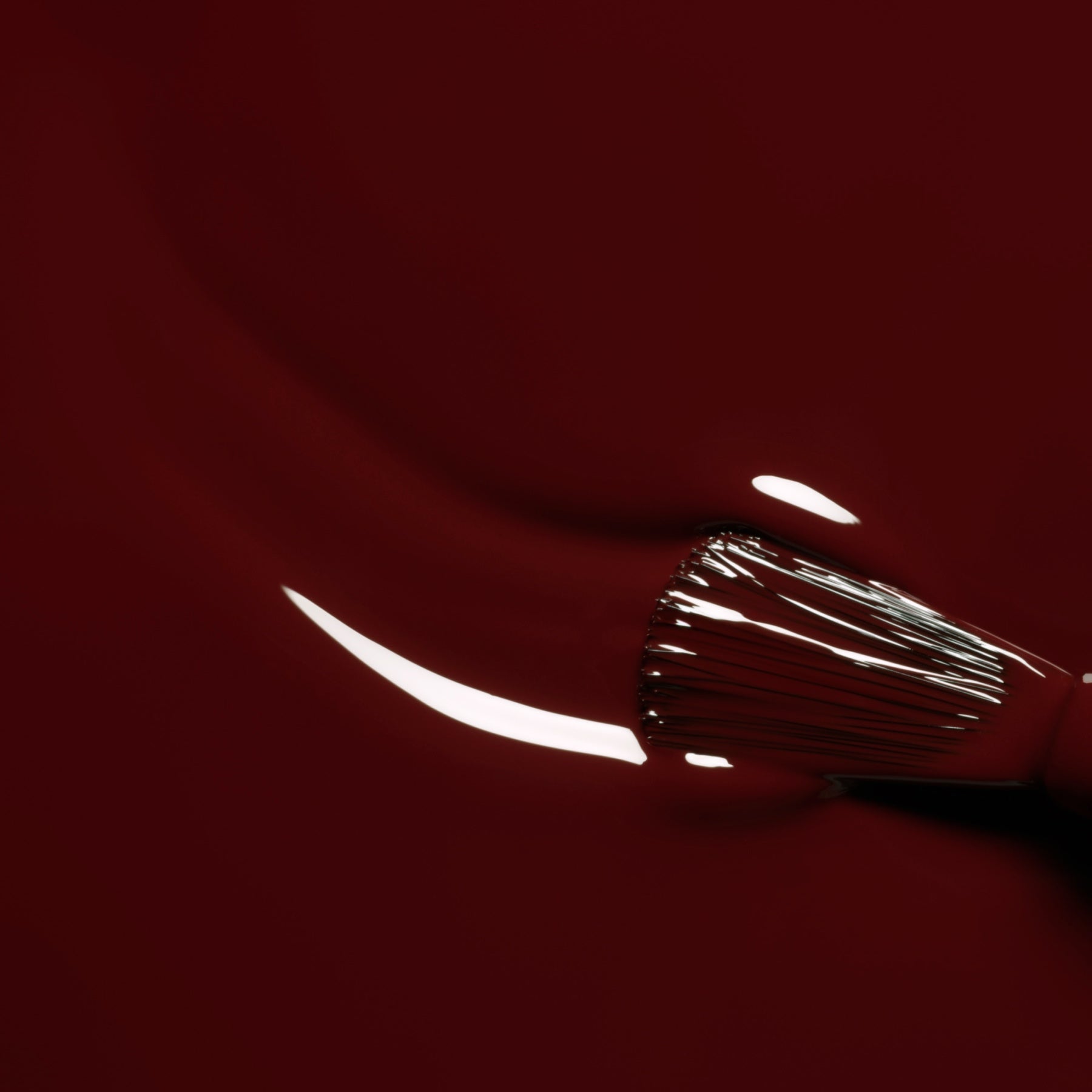 A close-up of a brush spreading Grenat, an earthy red nail polish from Manucurist’s Green™ range, with light reflecting off the smooth, glossy surface.
