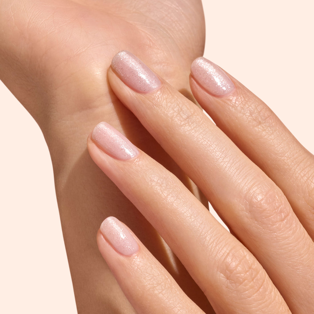 A hand with short, neatly manicured nails painted light pink and finished with Manucurist&