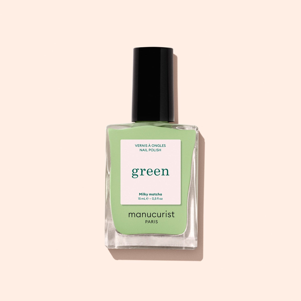 A bottle of Manucurist’s Milky Matcha nail polish, distinguished by its sleek black cap and delicate botanical hues, from The Green range, is displayed against a light beige background.