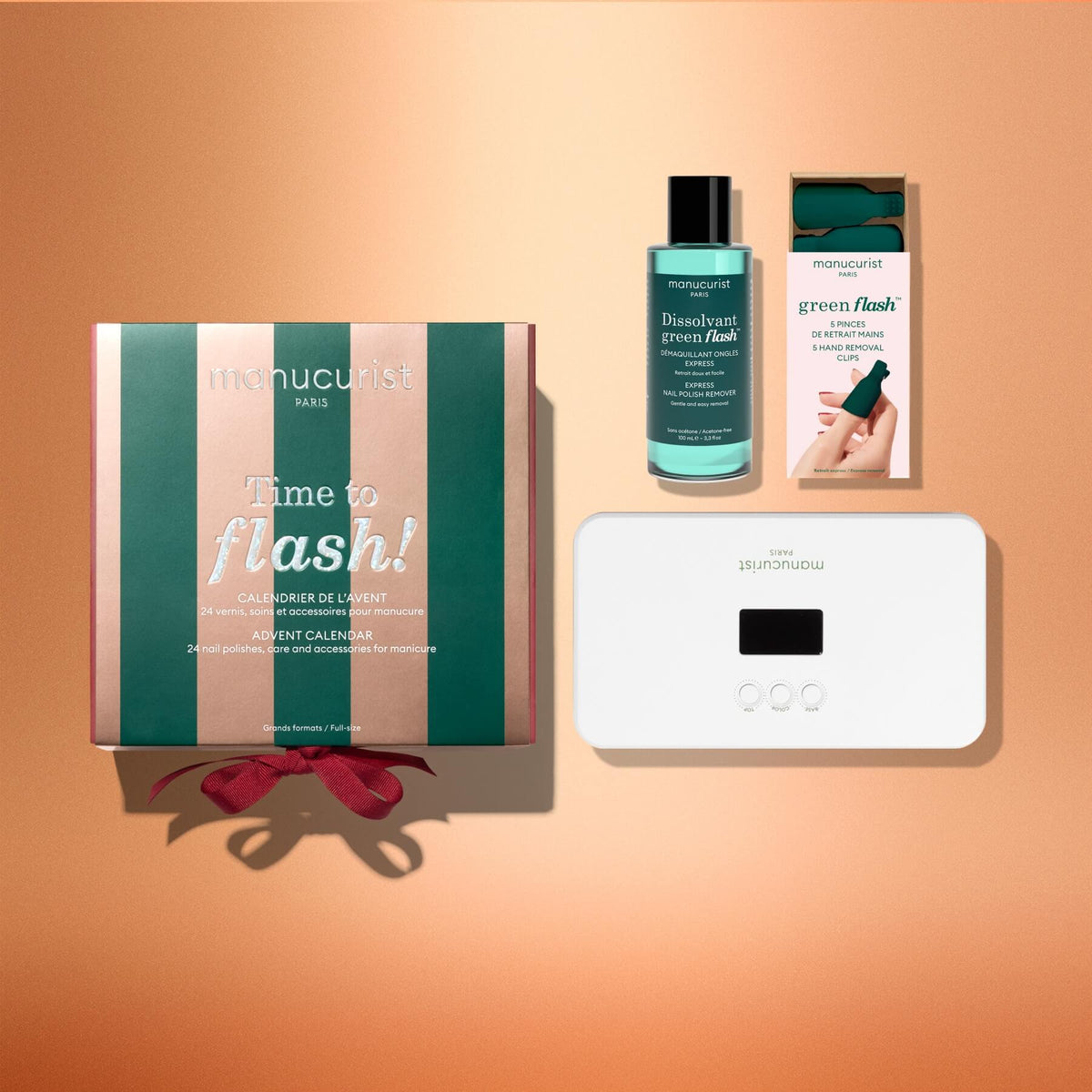Four Manucurist Advent Calendar Time to Flash! products are displayed on a peach background: a gift box, nail polish remover bottle, nail strips box, and a white LED lamp perfect for your next gel polish manicure, all arranged neatly with shadows.