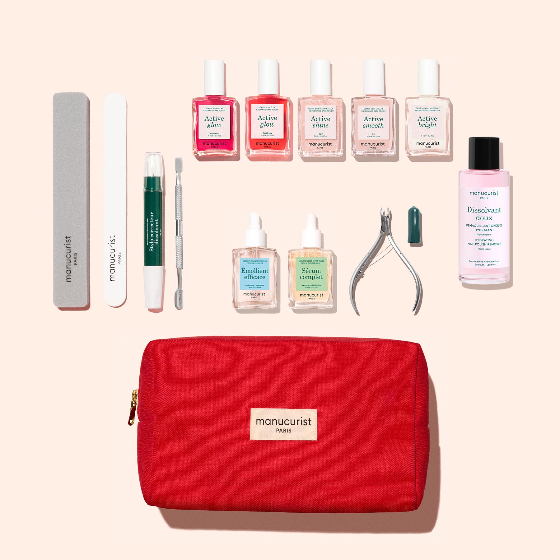 The Manucurist Active™ Super Ultimate Manicure Kit features a red zippered pouch surrounded by nail tools, cuticle oil, cuticle remover, and seven bottles of colorful nail polish—all neatly arranged on a light pink background—providing everything you need in a complete set for healthy nails.