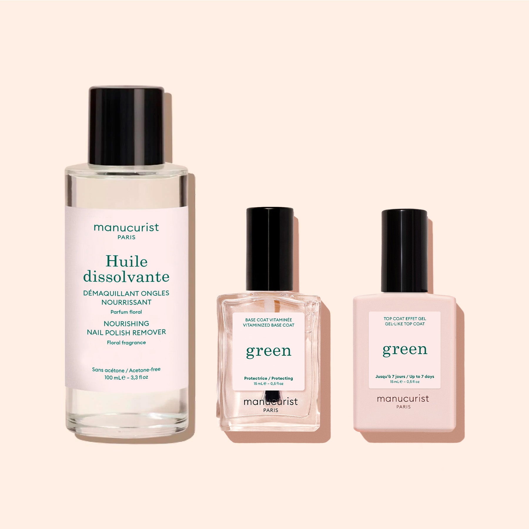 Three manicure products in clear bottles with black caps are arranged on a light pink background. Labels read Green Nail Polish Removing Oil from Manucurist, Base Coat, and Top Coat.