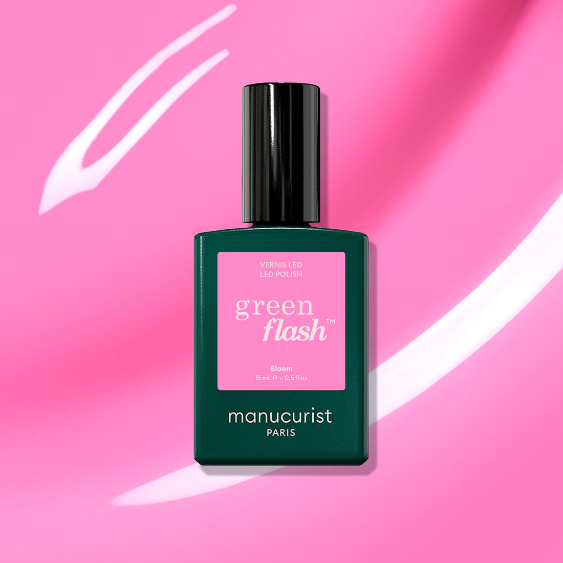 A bottle of Manucurist Bloom gel polish sits against a vibrant pink background with white streaks. The dark green bottle and pink label highlight the chic, magnetic intensity of this nail color.