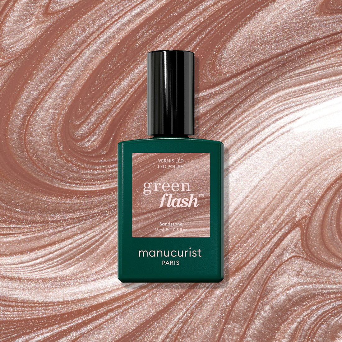 A bottle of Sandstone LED polish by Manucurist is displayed in front of a swirling, shimmering latte brown and beige background that matches the polish color.