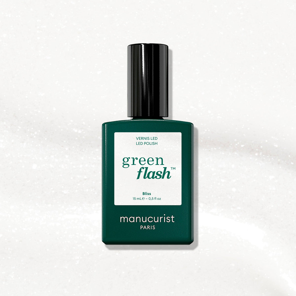 A green bottle of Manucurist gel polish in the shade Bliss rests on a white, slightly textured background. The label displays the shade name “Bliss” and indicates a size of 15 mL.