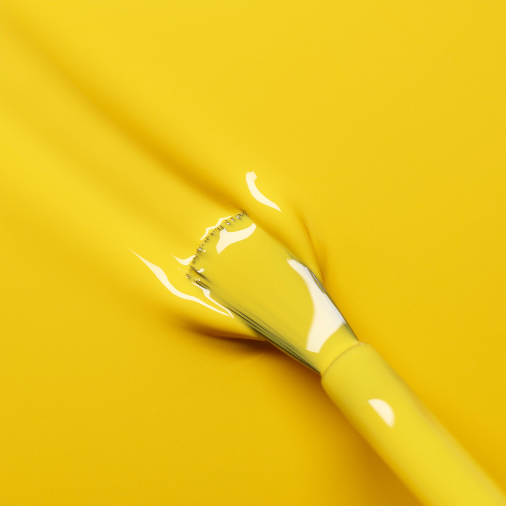 A Manucurist Gold Button brush with yellow bristles is coated in glossy yellow gel polish, blending into a bright background for a seamless, monochromatic look.
