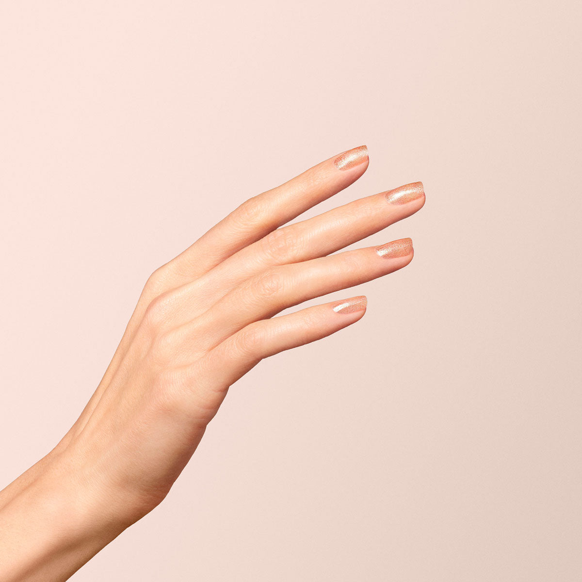 A close-up of a hand with fingers slightly apart, showcasing neatly manicured nails painted with Manucurist Gold nail polish against a plain, pale background.