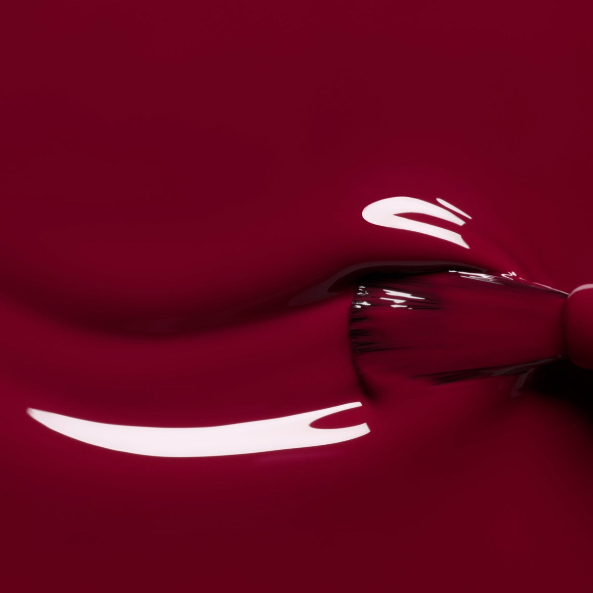 A close-up of a brush applying Manucurist’s Amour nail polish, a glossy and luminous burgundy shade, with smooth strokes and bright reflections visible on the surface.