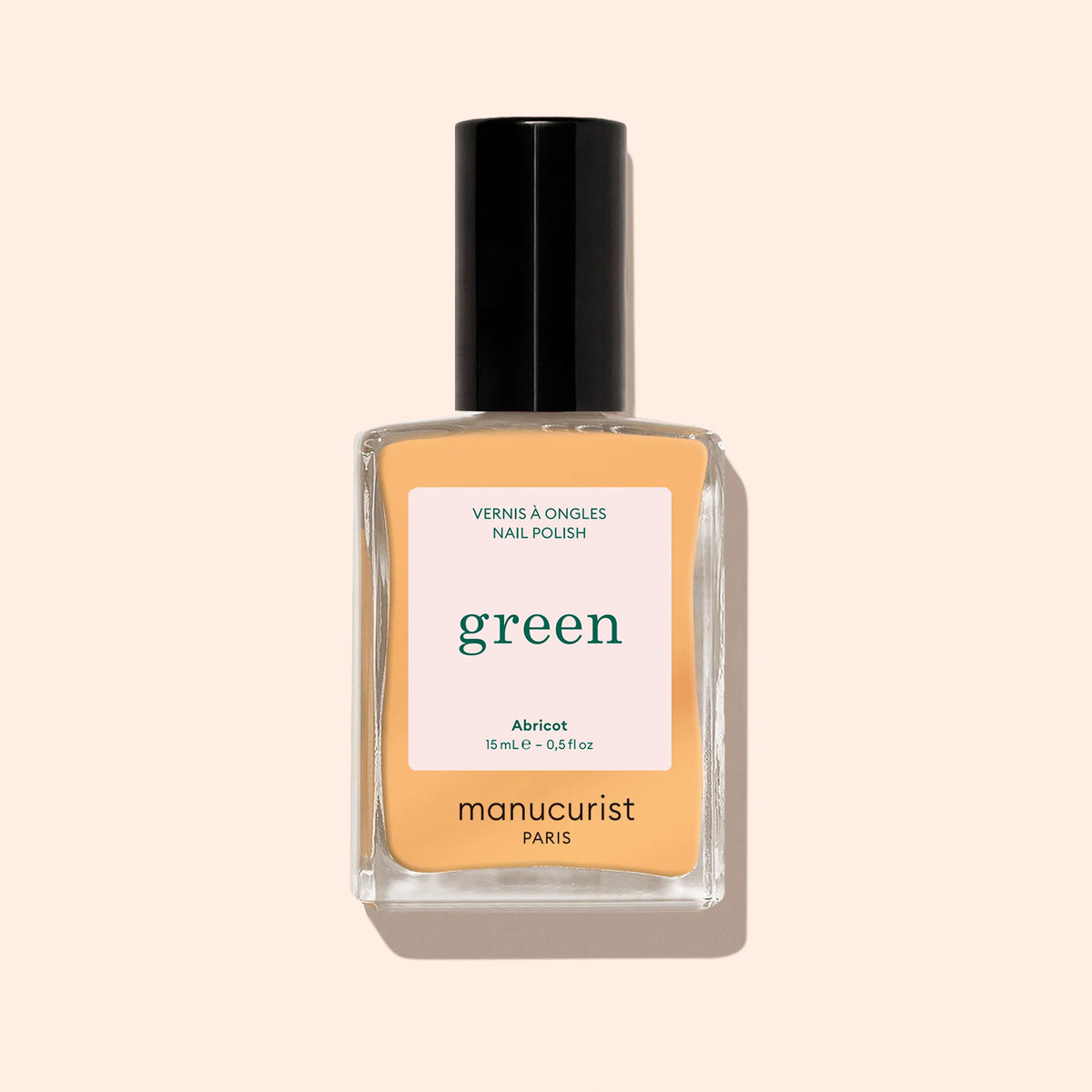 A bottle of Manucurist Abricot nail polish from the Green range in a peachy apricot shade, with a black cap, shown against a light beige background.