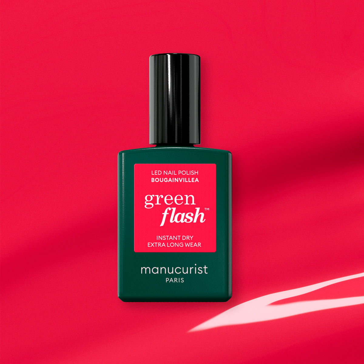 A bottle of Manucurist Bougainvillea gel polish, in a green bottle with a red label, is shown against a pink background with a white abstract design.