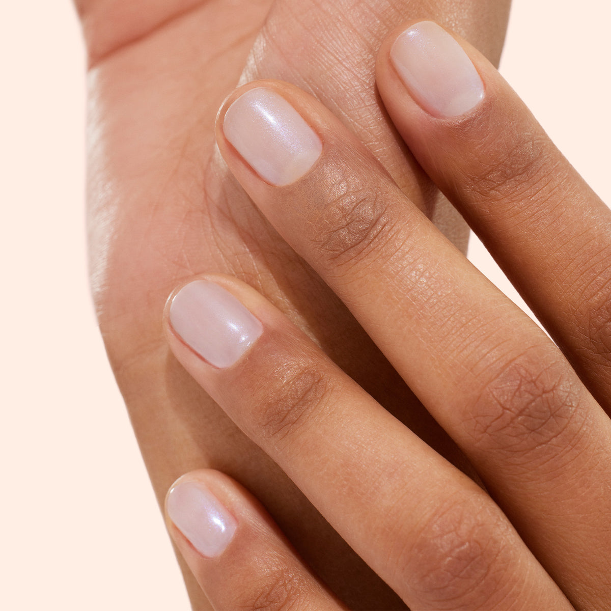 A close-up of a hand with neatly manicured nails painted in Manucurist’s Active™ Bright, a light, sheer, natural shade of bio-based nail polish, gently resting on the back of another hand. The background is a soft, neutral color.