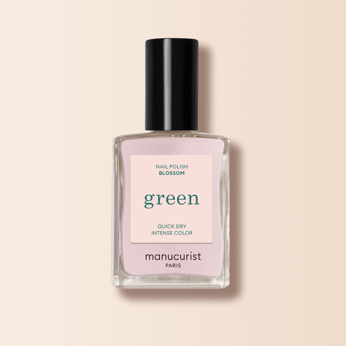 A bottle of Manucurist nail polish in the shade Blossom, with a light pink label and black cap, is displayed against a beige background.
