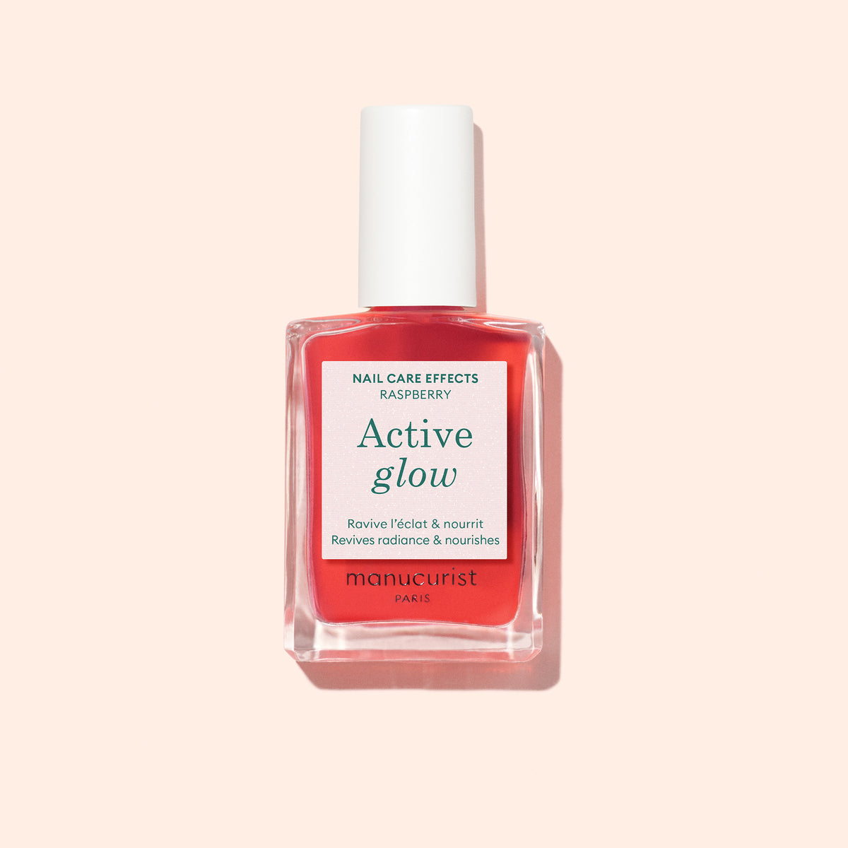 A bottle of Manucurist Active™ Glow Raspberry, with a white cap and pink label, is showcased against a light peach background—an elegant nail enhancer crafted to elevate your natural glow.