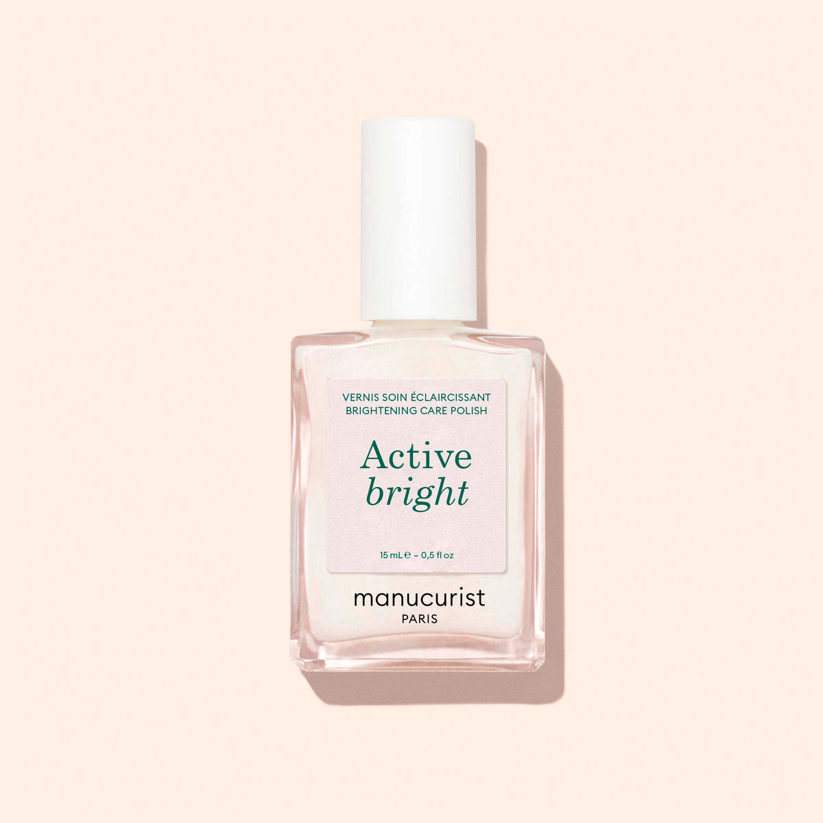 A clear glass bottle of Manucurist Active™ Bright bio-based nail polish and nail strengthener with a white cap, photographed against a light beige background.