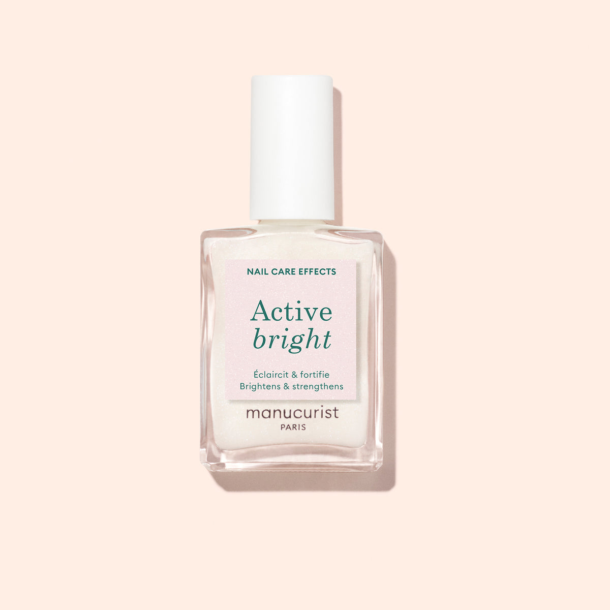 A clear glass bottle of Manucurist Active™ Bright bio-based nail polish and nail strengthener with a white cap, photographed against a light beige background.