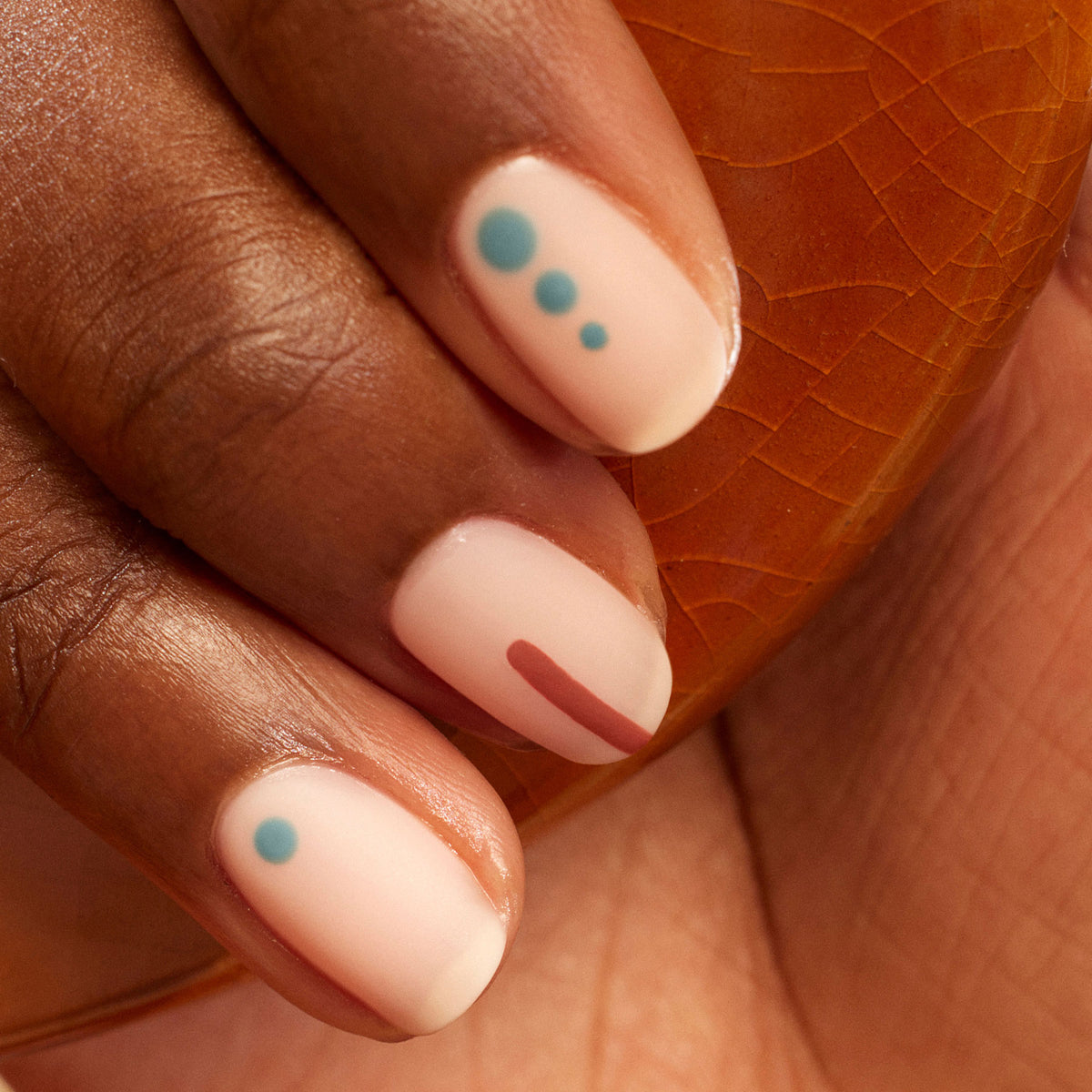 A close-up of a hand with short, almond-shaped nails painted in Sage from Manucurist&