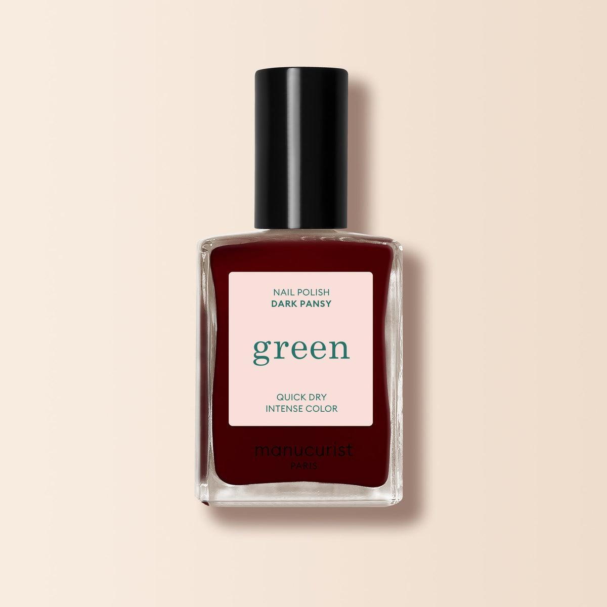 A bottle of Manucurist Dark Pansy nail polish in a deep burgundy shade, with a black cap and a “green, quick dry intense color” label.