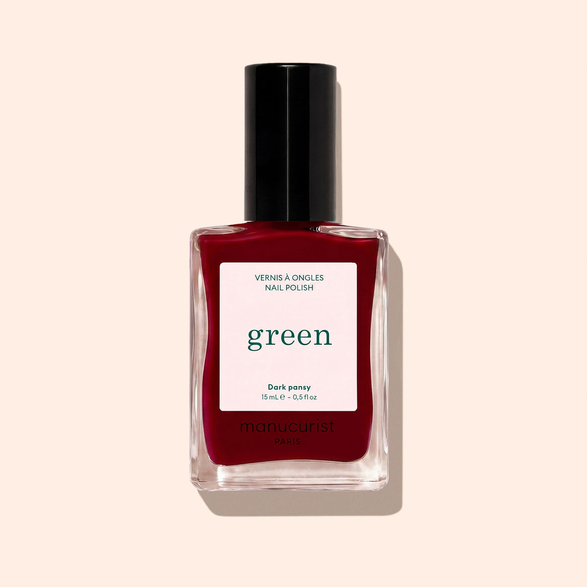 A bottle of Manucurist Dark Pansy nail polish in a deep burgundy shade, with a black cap and a “green, quick dry intense color” label.