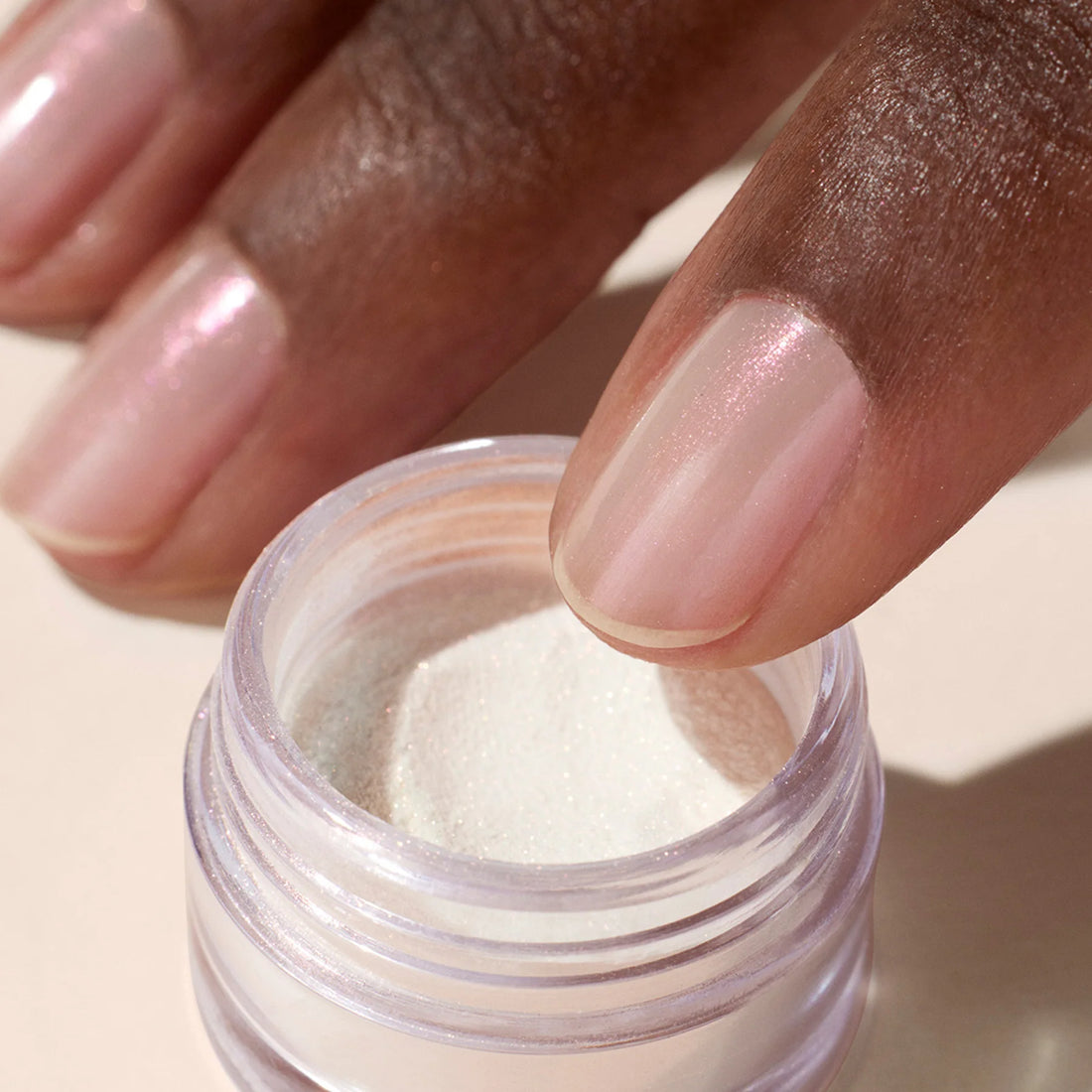 A close-up of a hand with neatly manicured, light pink nails dipping a finger into Manucurist&