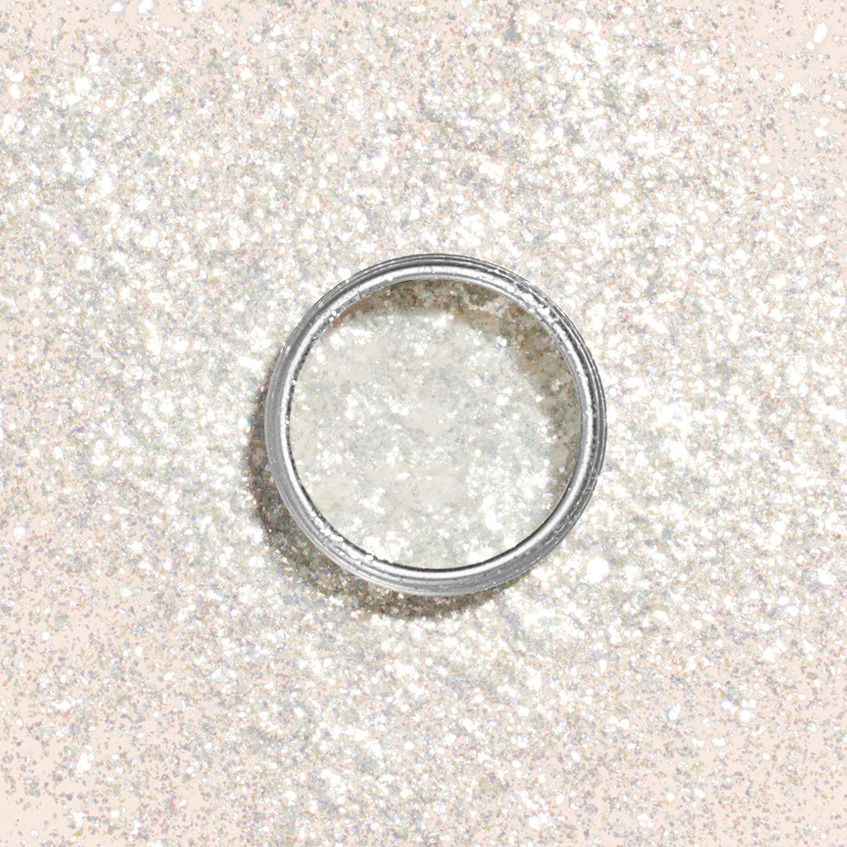 A round container of Manucurist Nacres Flakes—white, sparkly glitter with pearlescent flakes—rests on a matching shimmering surface, creating a dazzling backdrop perfect for adding flair to your next manicure.