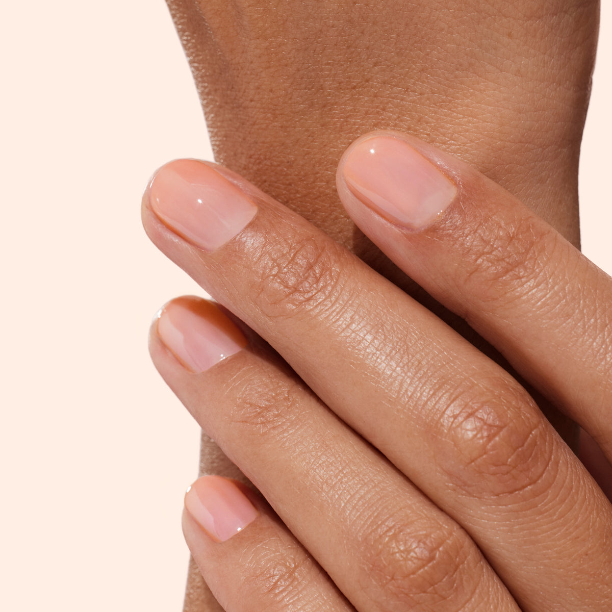 A close-up of a hand with natural, neatly manicured nails painted with Manucurist’s Active™ Glow Raspberry—a sheer, glossy nude polish—showcases the effects of dedicated nail care. The fingers, glowing with natural radiance, rest gently on the opposite wrist against a plain light background.