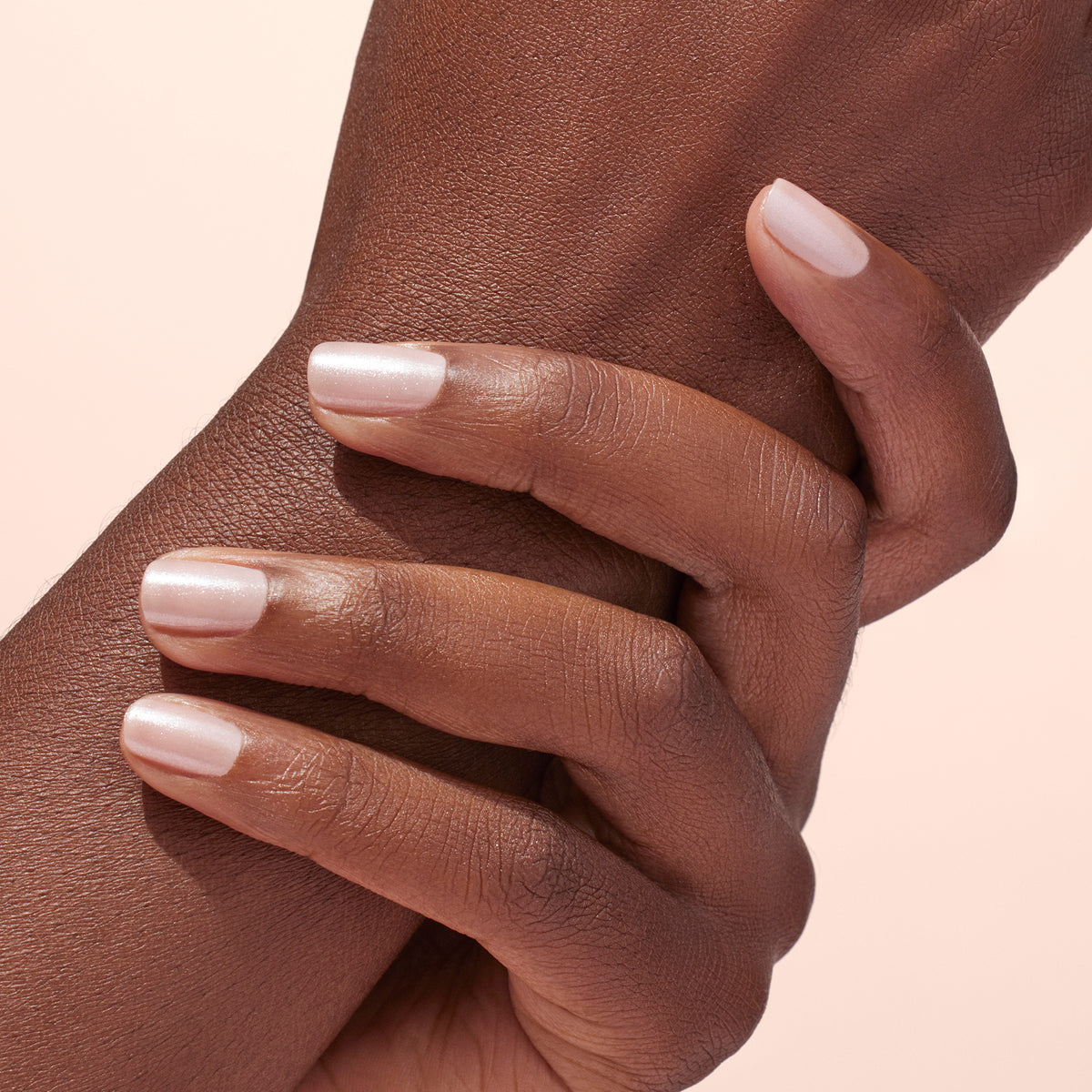A hand with neatly manicured nails displays a light pink polish topped with Manucurist White Glazed Effect Powder, creating a subtle shimmery look—ideal for glam manicure fans—against a soft, light background.