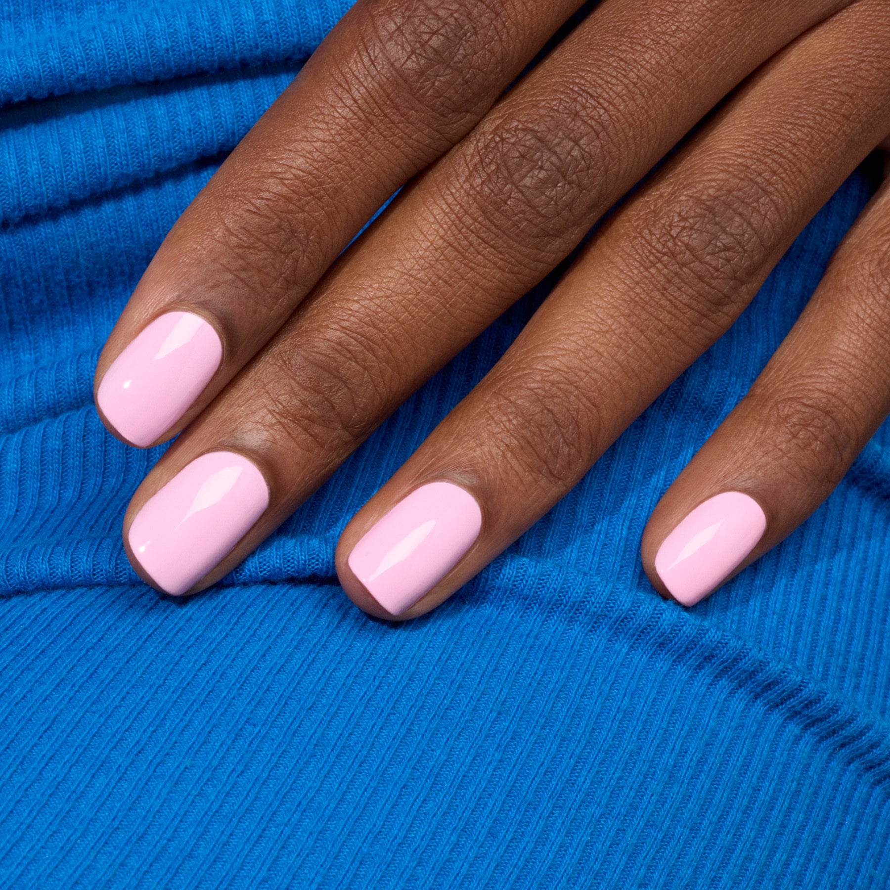 A hand with neatly manicured nails painted in the Manucurist shade "Candy" from the Green™ range rests on textured blue fabric.