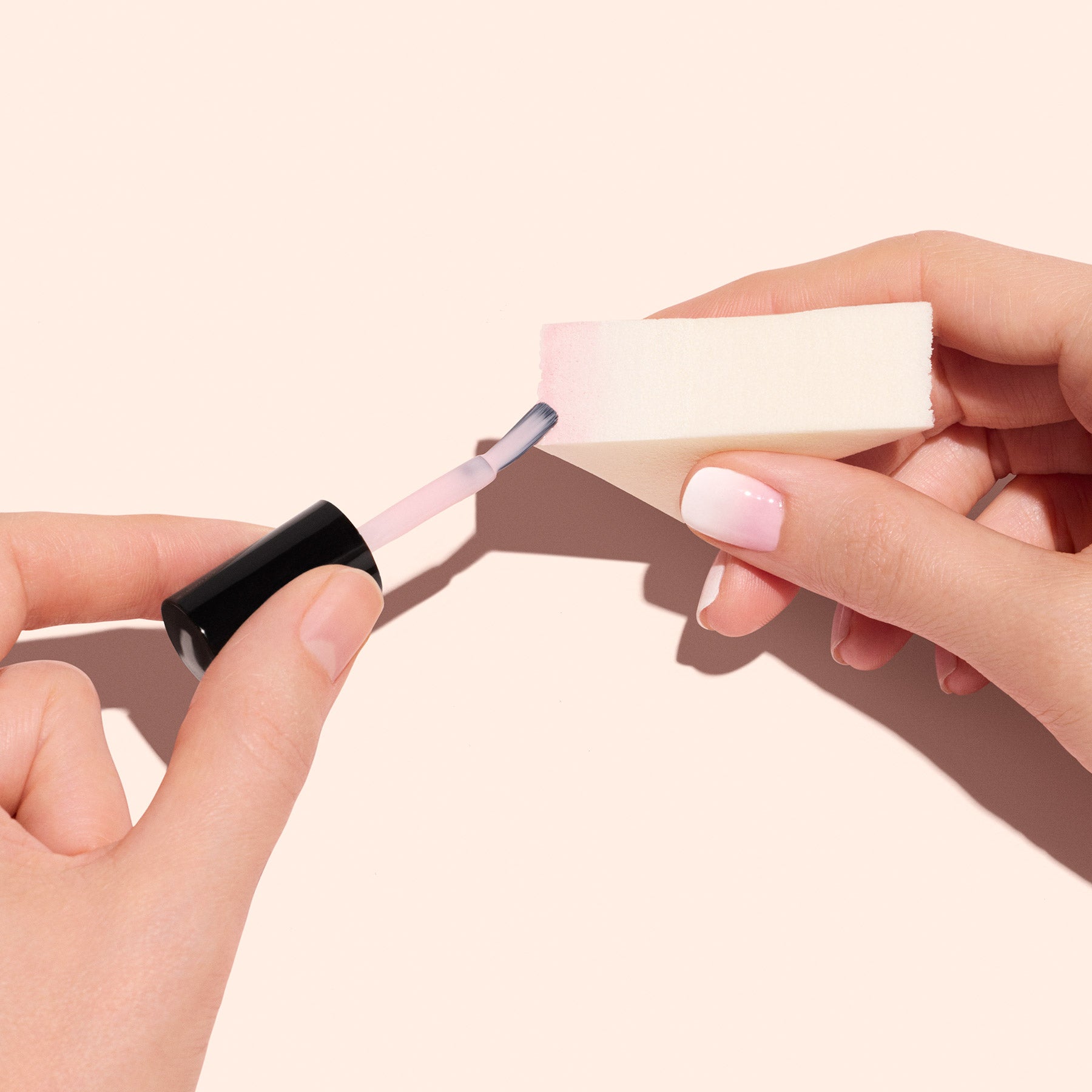 A person uses Manucurist Nail Art Sponges - x4 to apply light pink polish, creating gradient nails and showing off neatly manicured, pale pink nails against a neutral background.