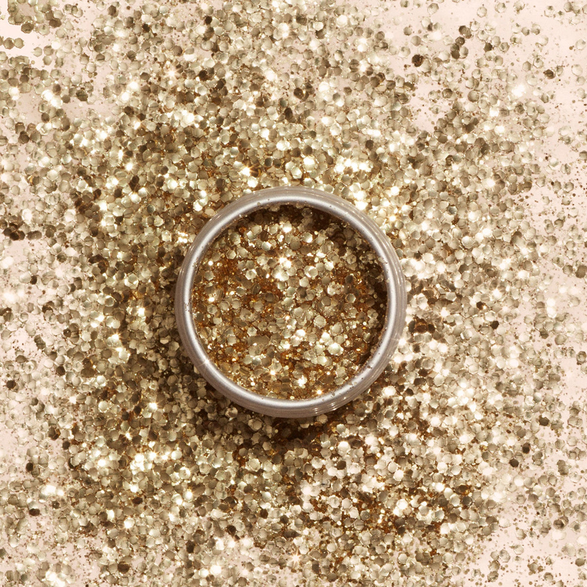 A silver ring lies on a surface sprinkled with Manucurist Biodegradable glitter, with extra glitter inside the ring. The sparkling display shines under the light, offering festive inspiration for nail art looks.