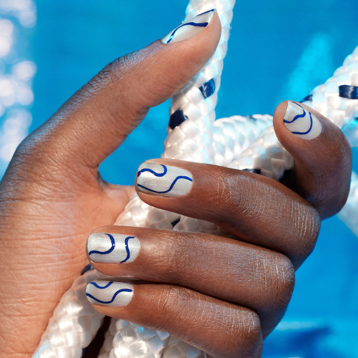 A hand with silver and blue wavy line nail art, created using Manucurist&