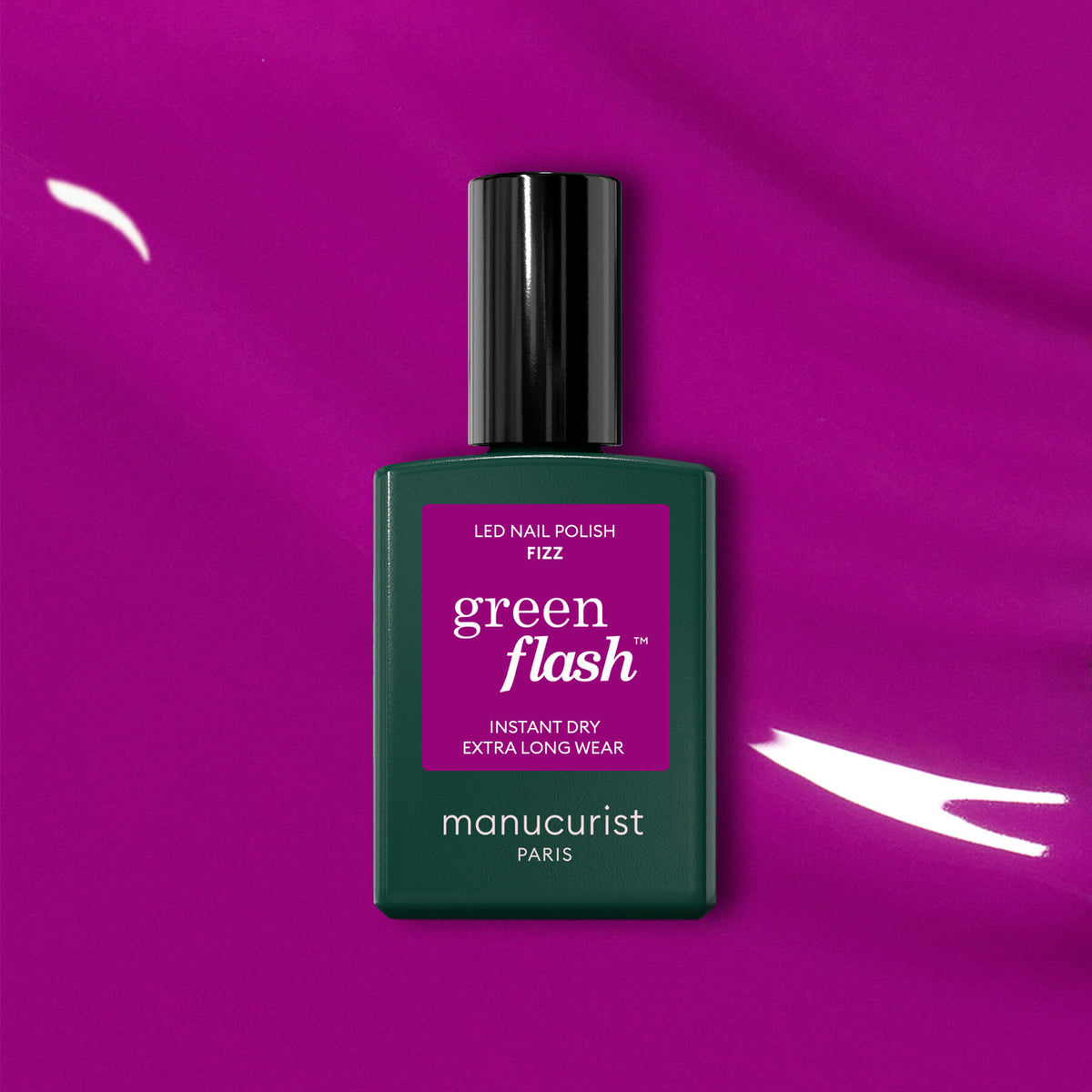 A bottle of Fizz nail polish by Manucurist, with magenta undertones and a dark green body plus a magenta label, sits on a vibrant magenta background accented by white brushstrokes.