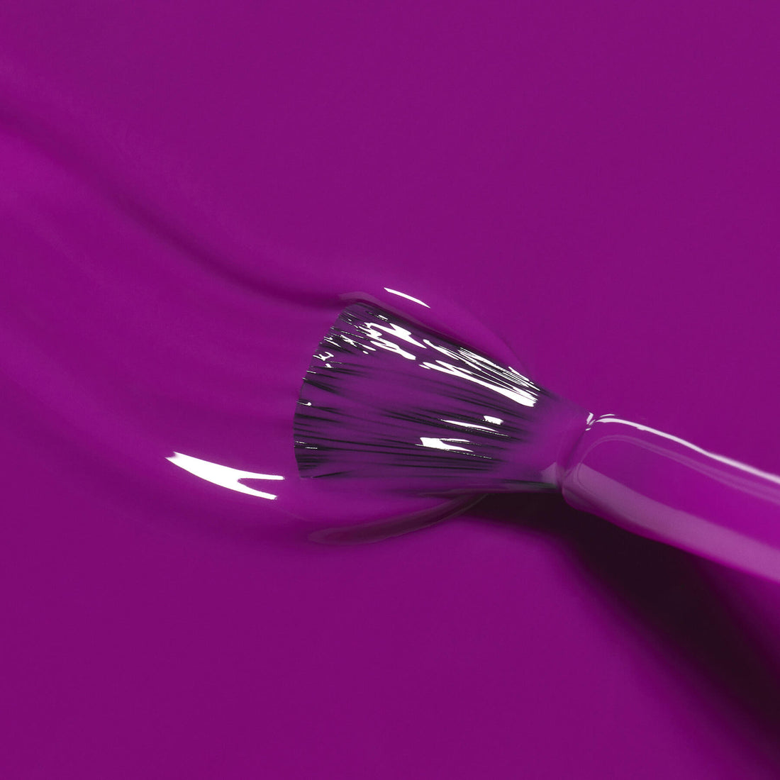 A close-up of a brush applying Manucurist’s Fizz, a glossy bright purple nail polish, onto a smooth surface, with the bristles clearly visible as they spread the vibrant color evenly.