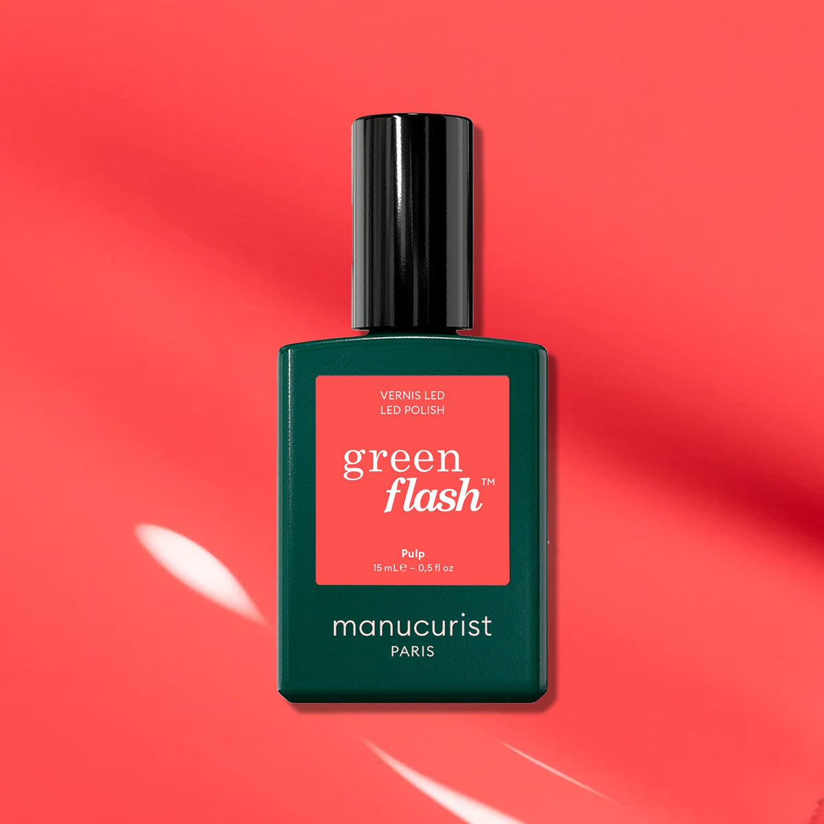 A green Manucurist Pulp Green Flash LED nail polish bottle rests on a vivid coral background, casting a soft shadow. The label features "Pulp," highlighting instant dry and extra-long wear—perfect for fans of coral pink gel polish.